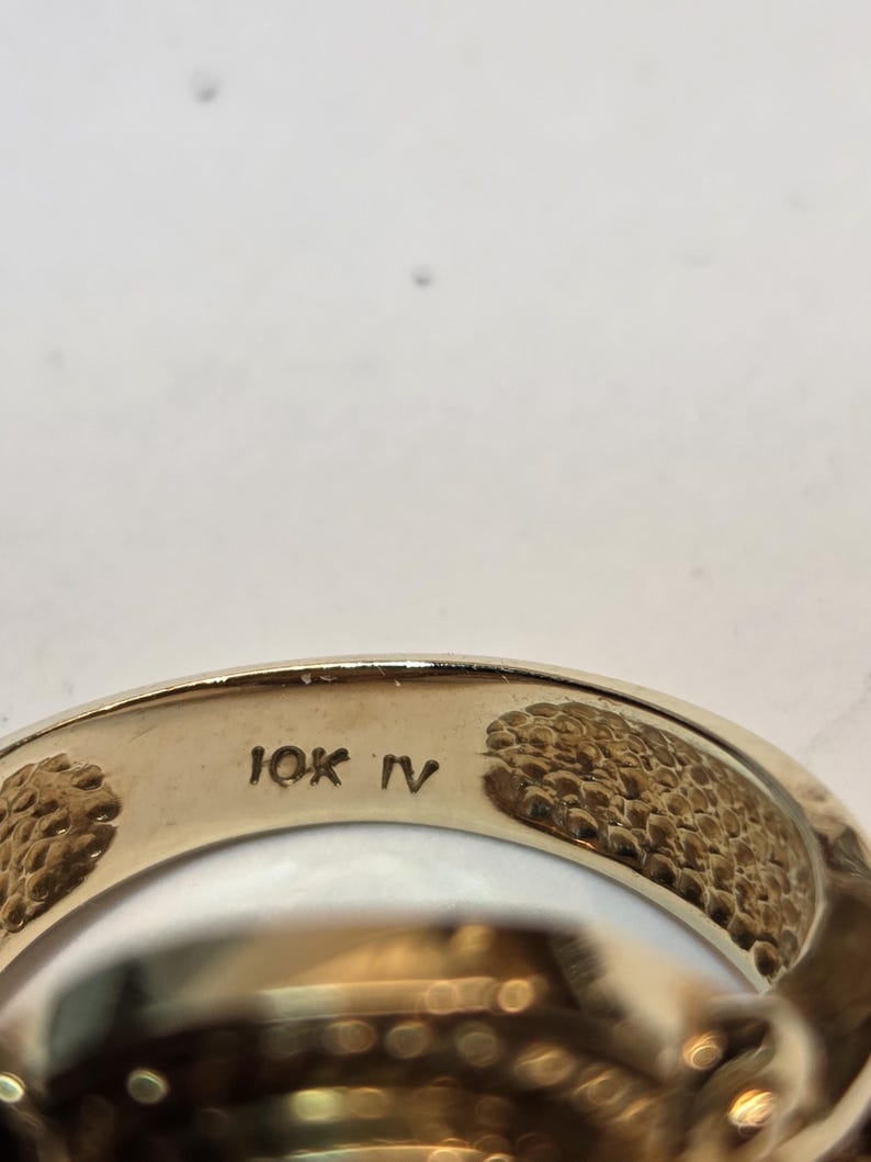 May include: Close-up of the inside of a gold ring with the inscription "10K IV" on the band.