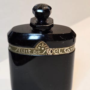 May include: A black glass bottle with a black glass stopper. The bottle has a gold and green label that reads "Nuit de Noel Caron".