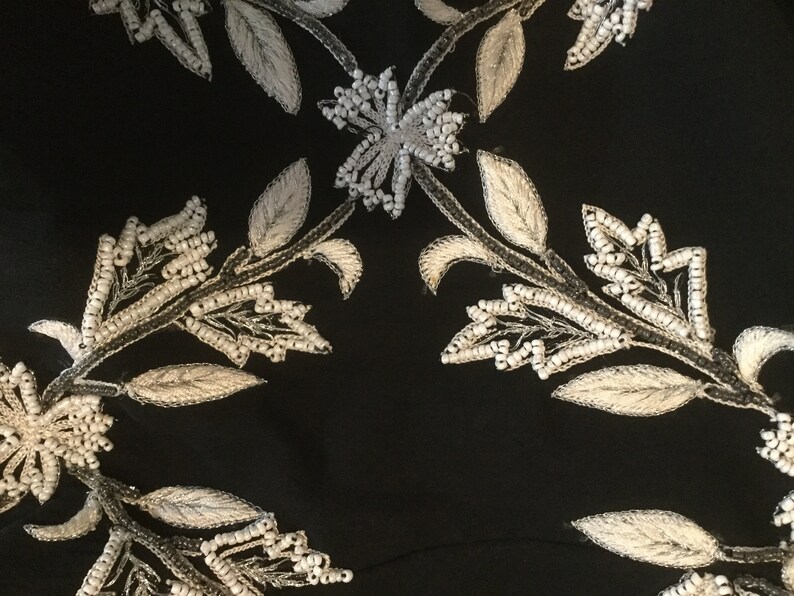 Puede incluir: Tela negra con bordado floral de cuentas blancas. El dise&ntilde;o presenta hojas y flores delicadas.