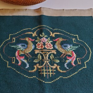 May include: A green needlepoint pillow with a floral design featuring two birds and a vase of flowers. The design is surrounded by a gold border.