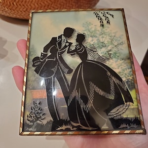 May include: A framed silhouette of a couple in a garden setting. The couple is dressed in formal attire and is holding hands. The background is a watercolor painting of a garden with trees and flowers.