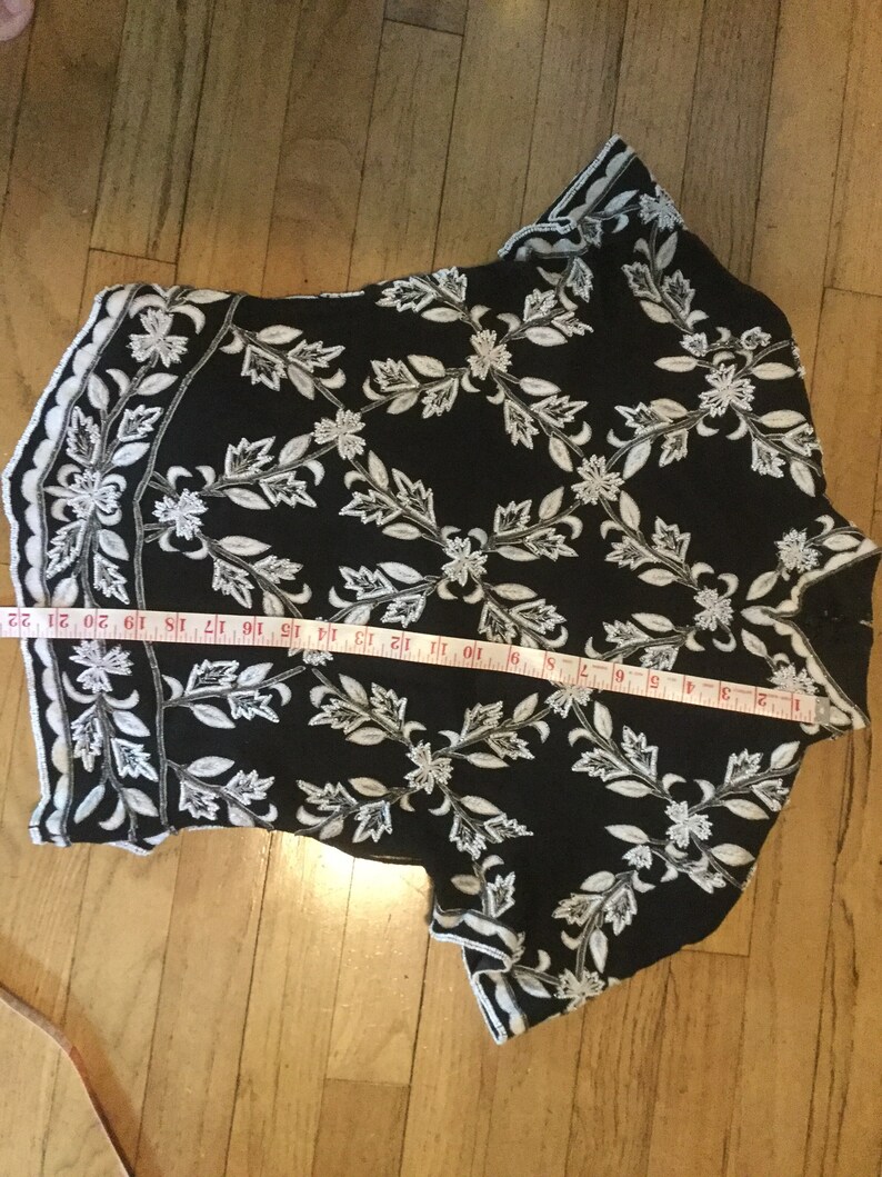 Puede incluir: Top negro y blanco bordado con un patr&oacute;n floral. El top tiene mangas cortas y un dobladillo festoneado.