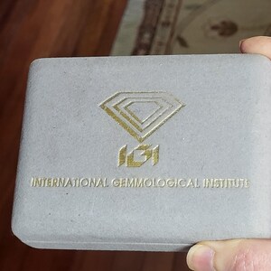 May include: A gray velvet box with the International Gemmological Institute logo in gold. The logo features a diamond shape with the letters IGI inside.