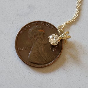 May include: A small, round, clear diamond pendant on a gold chain. The pendant is about the size of a US penny.