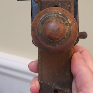 May include: A vintage door knob with a wooden handle and a brass trim. The knob is attached to a metal plate with a keyhole.