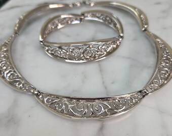 May include: A silver filigree necklace and bracelet set. The necklace and bracelet are both made of delicate, intricate silver filigree work. The necklace is a choker style and the bracelet is a bangle style.