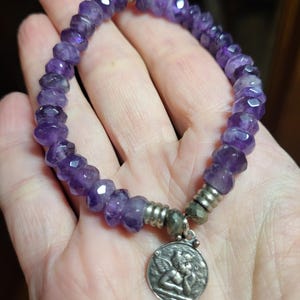 May include: Amethyst gemstone bracelet with a silver angel charm. The bracelet is made with faceted amethyst beads and has a silver clasp.