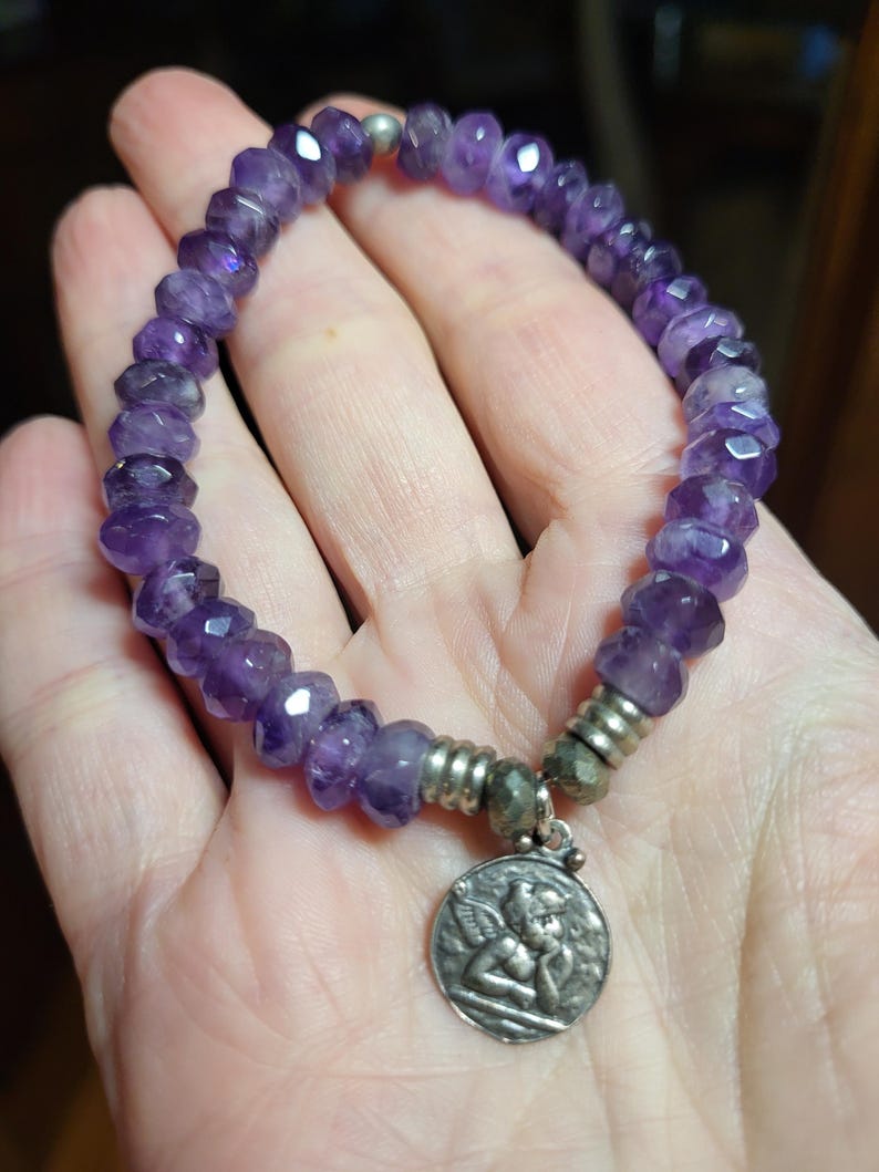 May include: Amethyst gemstone bracelet with a silver angel charm. The bracelet is made with faceted amethyst beads and has a silver clasp.