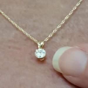 May include: A delicate gold chain necklace with a small, round, clear gemstone pendant.