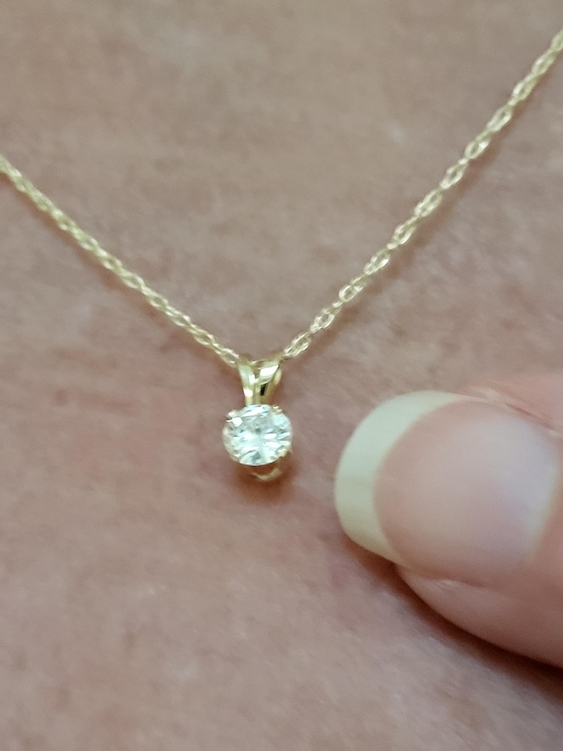May include: A delicate gold chain necklace with a small, round, clear gemstone pendant.