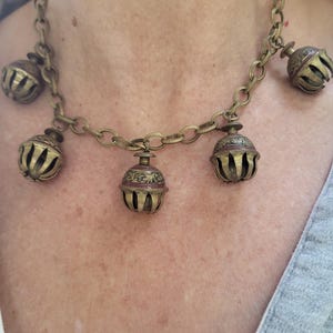 Pu&ograve; includere: Una collana a catena dorata con cinque ciondoli a forma di campana decorati. Le campane sono decorate con motivi intricati e hanno una patina marrone rossiccia.