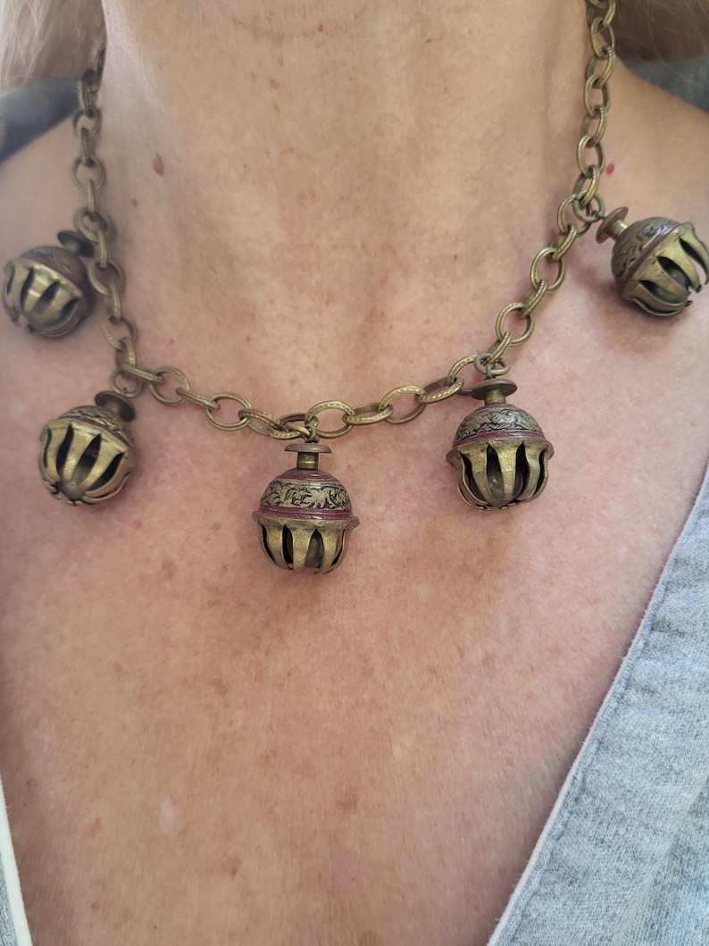 Pu&ograve; includere: Una collana a catena dorata con cinque ciondoli a forma di campana decorati. Le campane sono decorate con motivi intricati e hanno una patina marrone rossiccia.