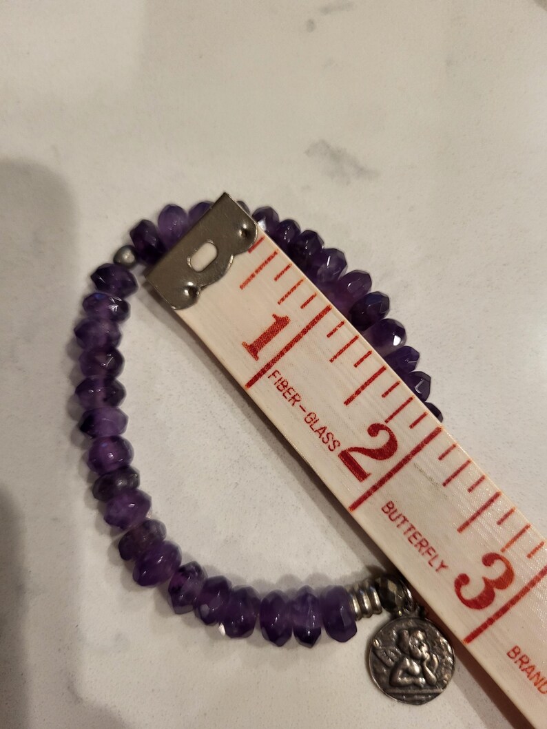 May include: A purple amethyst beaded bracelet with a silver charm featuring a butterfly design. The bracelet measures approximately 2 inches in diameter.