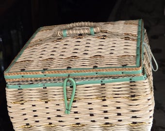 May include: A woven wicker box with a teal lid and gold accents. The box has a teal handle and teal feet.