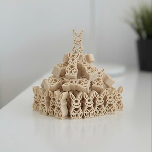 Op de afbeelding: Een decoratieve stapel beige blokken in de vorm van konijntjes. De blokken zijn gerangschikt in een piramidevorm, met een konijnenfiguur bovenaan. De blokken hebben een uitgesneden ontwerp en de algehele esthetiek is minimalistisch en modern.