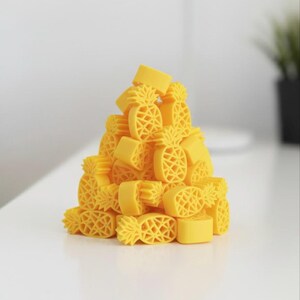 May include: A pile of yellow pineapple-shaped erasers. The erasers have a detailed design, with a textured surface and a pineapple crown. The erasers are stacked on a white surface, creating a playful and tropical theme.