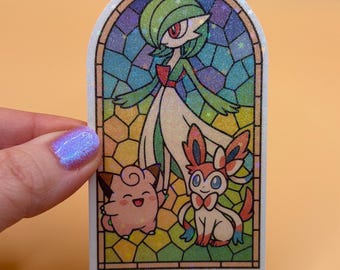 May include: A sticker featuring a stained-glass design with three Pokémon characters. The top character is Gardevoir, with green hair and a white dress. Below are Jigglypuff and Sylveon. The background is a mosaic of colorful glass.