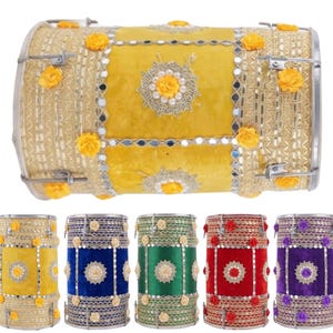 Op de afbeelding: Een verzameling decoratieve drums in verschillende kleuren, waaronder geel, blauw, groen, rood en paars. De drums zijn versierd met bloemaccenten, spiegels en metalen afwerking, wat een feestelijke en sierlijke uitstraling creëert.