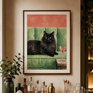 May include: A framed wall art print featuring a long-haired black cat resting on a green tufted sofa next to a pink cocktail in a glass. The background of the artwork shows a salmon-coloured wall above the sofa, presented in a wooden frame.