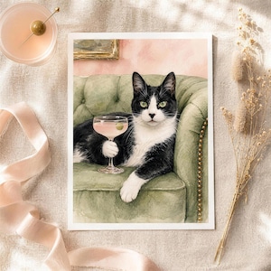 May include: A rectangular art print featuring a black and white cat with green eyes sitting on a tufted sage green sofa. The cat holds a stemmed cocktail glass containing a pink liquid and a single green olive. The background is a soft pink wall.