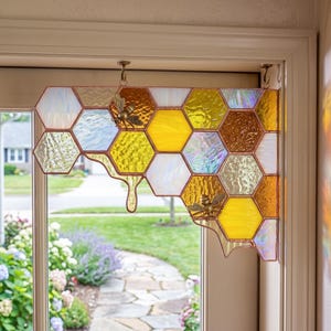 Peut inclure: Un panneau en vitrail en forme de nid d'abeilles composé de pièces hexagonales dans des tons de jaune, ambre et blanc irisé. Le panneau comprend deux petites figurines d'abeilles en métal fixées au verre et est suspendu par deux crochets.