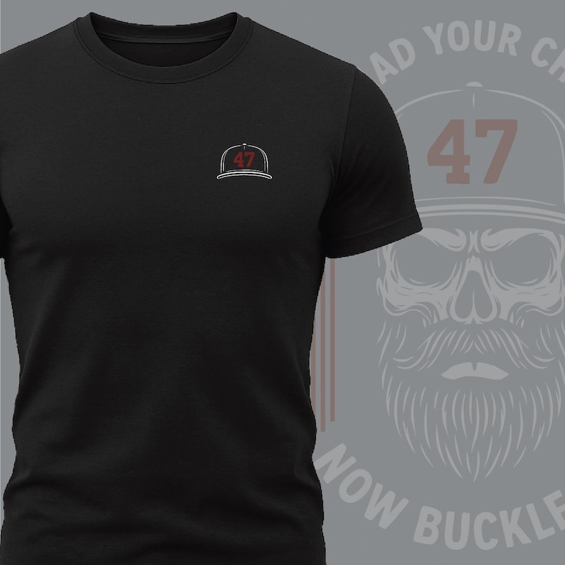 Pode incluir: Camiseta preta de gola redonda com um pequeno logotipo bordado de bon&eacute; de beisebol no peito. O logotipo apresenta o n&uacute;mero "47" em vermelho. Um gr&aacute;fico no lado direito mostra uma caveira usando um bon&eacute; de beisebol com o n&uacute;mero "47" e o texto "AD YOUR CH NOW BUCKLE".