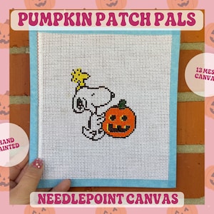 May include: A white needlepoint canvas featuring a hand-painted design of Snoopy with Woodstock and a jack-o'-lantern. The canvas has blue taped edges and is labeled 13 mesh canvas. The text PUMPKIN PATCH PALS and NEEDLEPOINT CANVAS is visible.