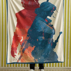 May include: A cream-coloured blanket featuring a red and blue artistic rendering of two figures with swords. The figures are set against a backdrop of orange and blue paint splatters. The blanket has a dark blue border.
