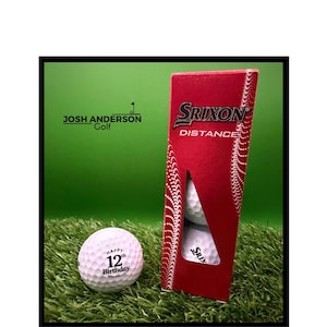 May include: A white golf ball with the text Happy 12th Birthday printed in black, positioned next to a red Srixon Distance golf ball box containing two additional golf balls. The box features white dotted patterns and the Josh Anderson Golf logo.