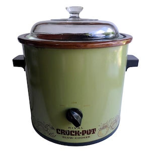 May include: A vintage Rival Crock-Pot slow cooker in a light green color. It has a glass lid, a wooden rim, and a black control knob with settings for off, low, and high. The words "Crock-Pot" and "Slow-Cooker" are printed on the front.