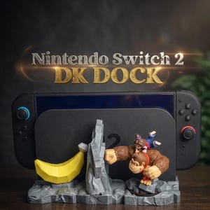 May include: A black Nintendo Switch 2 DK Dock with a Donkey Kong theme. The dock features a banana, a rocky structure, and a Donkey Kong figure with Diddy Kong riding on his back. The text "Nintendo Switch 2 DK DOCK" is displayed above.