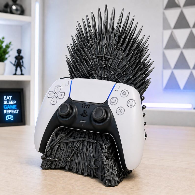 Pode incluir: Um suporte de comando preto em forma de trono, com um encosto alto de l&acirc;minas pontiagudas. Um comando de jogo sem fios branco e preto repousa firmemente no centro da base escura e texturada, decorada com um padr&atilde;o de espadas.