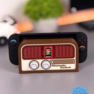 May include: A Nintendo Switch console docked in a brown and cream-colored retro radio-style case. The case has a red mesh speaker design and the words "Nintendo Switch" are printed on the front. A game cartridge is inserted.