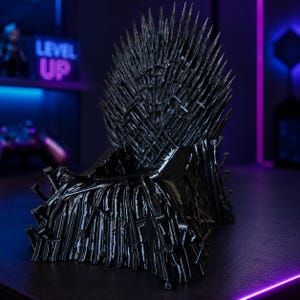 Pode incluir: Uma r&eacute;plica em miniatura preta e brilhante de um trono constru&iacute;do a partir de numerosas l&acirc;minas de espada. A estrutura apresenta um encosto alto e pontiagudo composto por punhos e l&acirc;minas de espada verticais e cruzadas, com base de metal.
