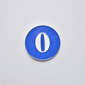 May include: A blue and white enamel pin in the shape of the number zero. The pin has a circular blue border with a white oval in the center. The pin is set against a white background.