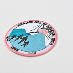 May include: Circular patch with a pink border featuring a blue mountain scene, a rising sun, and silhouettes of people. The text "JACK AND JILL OF AMERICA INC." and "1938" are also included.