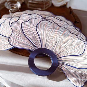 May include: A set of fan-shaped paper placemats featuring a white background with intricate, radiating lines in navy blue, red, and tan. Each placemat has a scalloped edge and a circular navy blue cutout at the base, creating a layered, fan-like appearance.