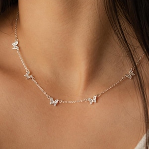 Peut inclure: Un collier à chaîne de couleur argentée orné de plusieurs petits pendentifs en forme de papillon espacés régulièrement. Chaque papillon est agrémenté de minuscules pierres transparentes et scintillantes incrustées dans les ailes métalliques.