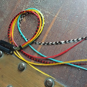 May include: A set of colorful feather hair extensions with a black clip. The extensions are red, yellow, blue, and black.
