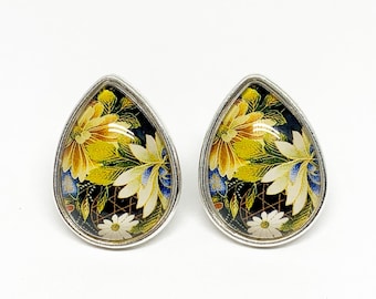 May include: A pair of silver teardrop-shaped earrings with a floral pattern in shades of yellow, white, and blue on a black background.
