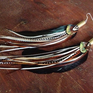 8 to 9” long feather earrings with natural shades and bullet cap tops.  Fatter iridescent green black feathers at the back with thinner natural shades and grizzly on the front with peacock top embellishment