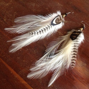 May include: A pair of feather earrings with white and brown feathers. The earrings have a simple design and are perfect for adding a touch of bohemian style to any outfit.