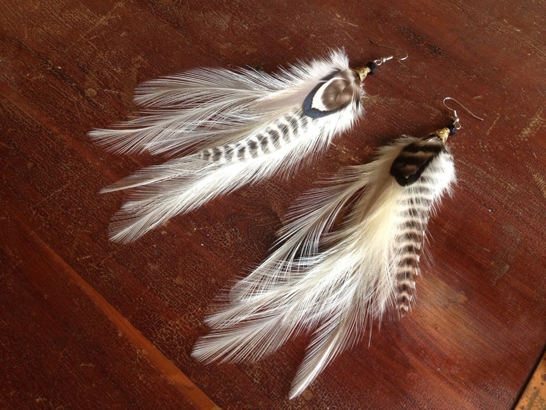 May include: A pair of feather earrings with white and brown feathers. The earrings have a simple design and are perfect for adding a touch of bohemian style to any outfit.