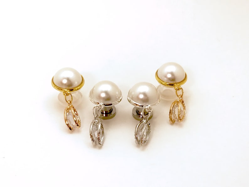 May include: Three pairs of pearl earrings with dangling crystal charms. The earrings are available in gold, silver, and rose gold.