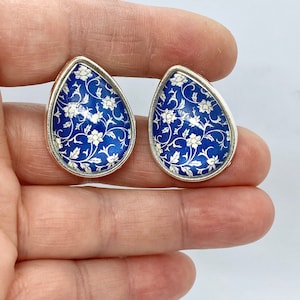 Puede incluir: Un par de pendientes de plata en forma de lágrima con un patrón floral azul y blanco.