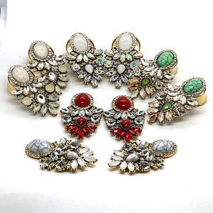 May include: Assortment of statement earrings featuring various gemstone colors and crystal accents. The earrings are made with gold-tone metal and feature a variety of shapes and sizes.