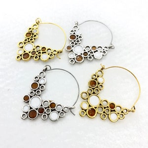 May include: Three pairs of hoop earrings with a geometric design. The earrings are made of silver and gold metal and feature a cluster of white and brown circles.