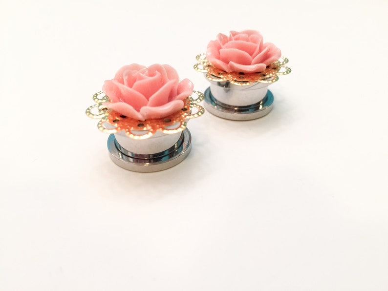 K&ouml;nnte beinhalten: Ein Paar silberne Ohrdehner mit rosa Rosenakzenten und goldenen Filigranen. Die Rosen haben eine glitzernde Oberfl&auml;che.
