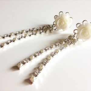 Puede incluir: Un par de pendientes colgantes de rosa blanca con detalles de cristal y perla.