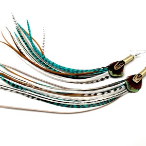 Può includere: Un paio di orecchini lunghi con piume in un'armonia di colori turchese, bianco e marrone. Gli orecchini sono realizzati con un bossolo di proiettile in ottone e presentano un piccolo accento di piuma di fagiano.